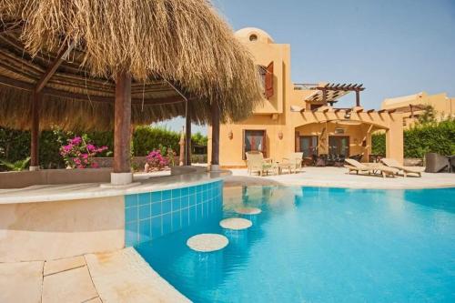 a house with a swimming pool with a straw roof at Y 140 wast golf heated private pool in Hurghada