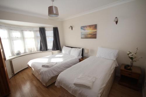 two beds in a room with white sheets at Deane House in Ruislip