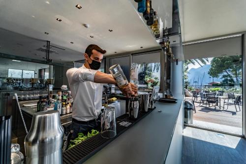 Ein Mann mit Maske macht einen Drink an einer Bar. in der Unterkunft Lake Front Hotel Mirage in Riva del Garda