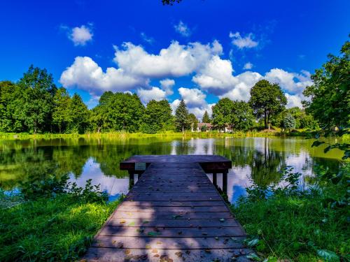 a wooden bridge over a lake with trees and clouds at Apartamenty Niebo in Kowary