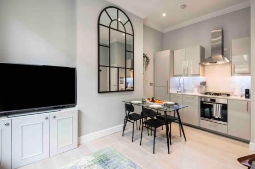 a kitchen with a table with chairs and a flat screen tv at Bright and Modern Bayswater Apartment in London
