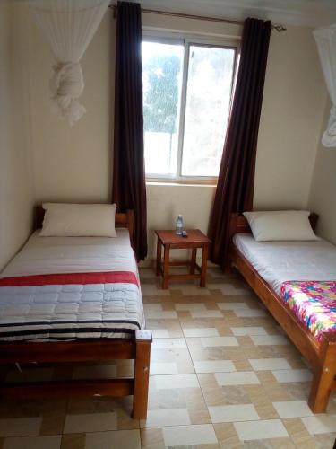 zwei Betten in einem Zimmer mit zwei Fenstern in der Unterkunft Dich Comfort Hotel University Branch in Gulu
