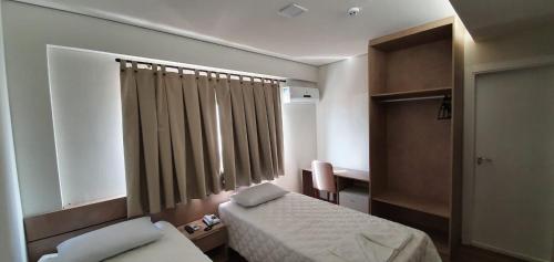 a small bedroom with a bed and a window at Hotel Fatti in Maringá