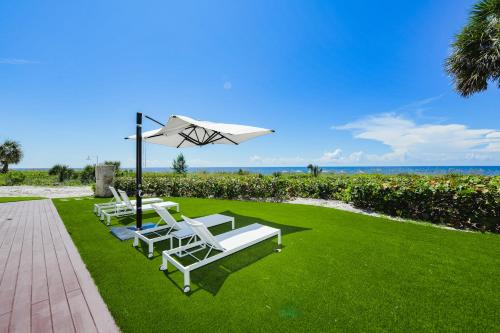 two white lounge chairs and an umbrella on a lawn at Casey Key Resorts - Beachfront in Venice