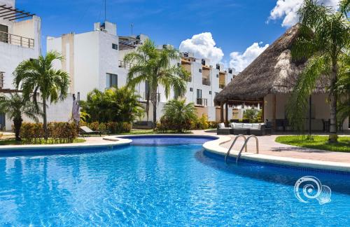 a pool at a resort with palm trees and buildings at Villa Ana Lucía. in Playa del Carmen