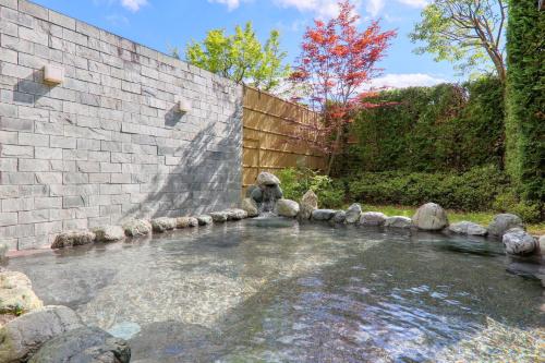 a pool of water with rocks in front of a brick wall at Fuji Matsuzono Hotel in Yamanakako
