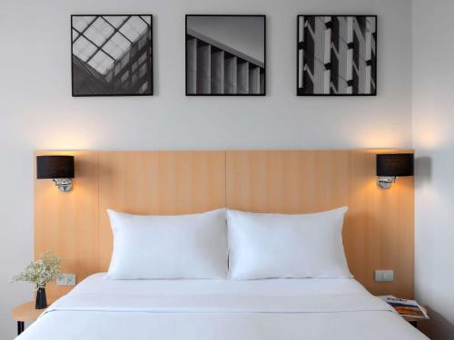 a bedroom with a white bed with four pictures on the wall at Ibis Bangkok Sukhumvit 4 in Bangkok
