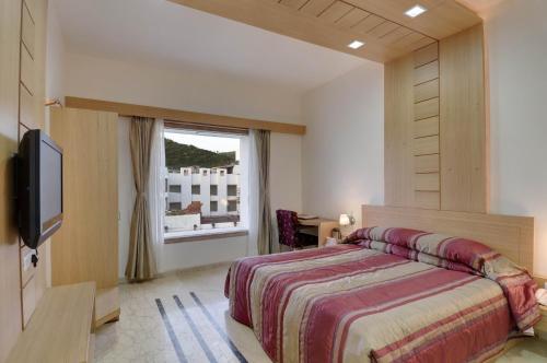 Un dormitorio con una cama y un televisor y una ventana. en Inder Residency Resort & Spa Udaipur, en Udaipur