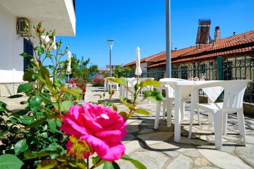 a patio with white tables and chairs and a pink rose at Kritikos Apartments in Pyrgadikia