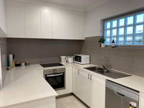 a kitchen with white cabinets and a sink at Chic 2Bed Close Airport Shops NETFLIX WIFI WINE in Perth