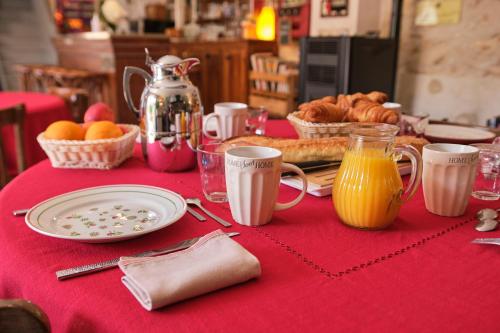een tafel met een rood tafelkleed, gevuld met ontbijtproducten en sap bij LES OLIVANIES in Monthelon