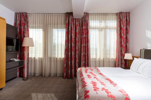 ノイ・イーゼンブルクにあるホリデイ イン フランクフルト エアポート - ノイ-イーゼンブルクのベッドと赤いカーテンが備わるホテルルームです。