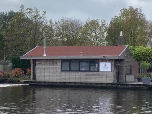 a house on a dock next to a body of water at Aangenaam op de Rijn, woonboot, inclusief privé sauna in Alphen aan den Rijn