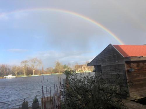 a rainbow over a house next to a body of water at Aangenaam op de Rijn, woonboot, inclusief privé sauna in Alphen aan den Rijn