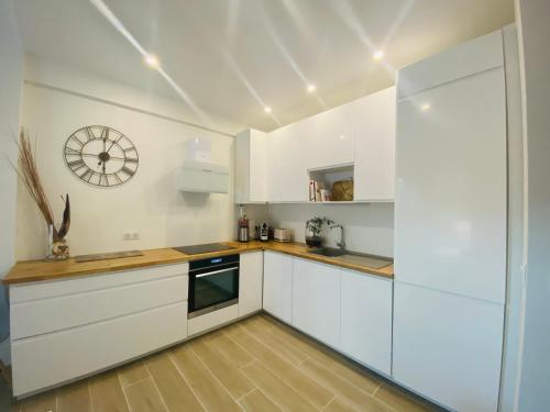une cuisine avec des placards blancs et une horloge murale dans l'établissement 50m plage - 2 pièces jardin garage, à Cagnes-sur-Mer