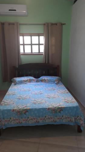 a bedroom with a bed with a blue comforter and a window at Suites Manu in Ilhabela