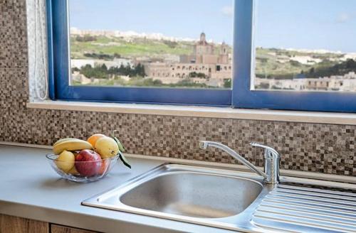 a bowl of fruit on a kitchen counter next to a sink at Ir-Rixa Holiday Penthouse in Għajnsielem