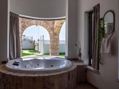 eine große Badewanne in einem Zimmer mit offenem Fenster in der Unterkunft סוויטות אושר בגולן in Had Nes