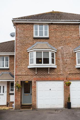 a brick house with two white garage doors at Beautiful Town House with Private Garden and Patio in Canford Magna