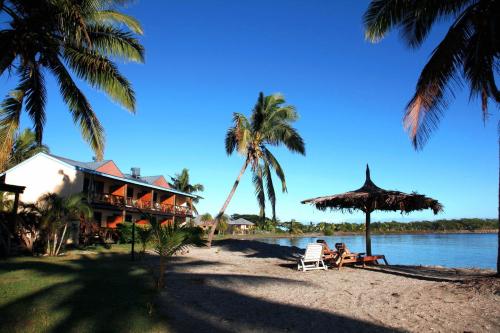 una casa en la playa con palmeras y gente sentada en sillas en Club Fiji Resort, en Nadi