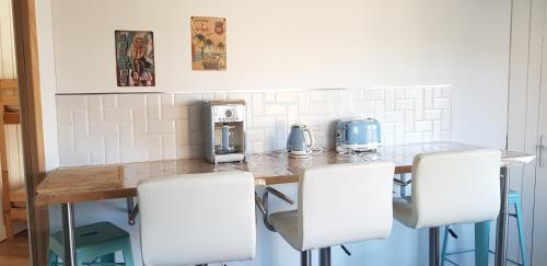 a kitchen with a counter with four white chairs at Les 3 mômes in Pontorson