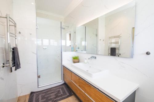 uma casa de banho branca com um lavatório e um chuveiro em Ten Whale Rock Gardens em Plettenberg Bay
