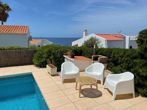 un patio con sillas blancas y una piscina en BiniVento- Lovely villa with pool near the beach en Binibeca