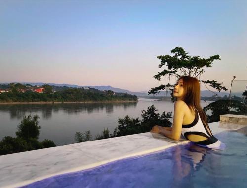 a woman sitting on a ledge with a surfboard at Chiangkhong Teak Garden Riverfront Onsen Hotel- SHA Extra Plus in Chiang Khong