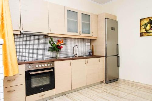 a kitchen with white cabinets and a stainless steel refrigerator at Cozy flats in an olive grove by the sandy beach in Kánalos