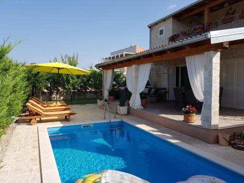 a swimming pool with an umbrella and a house at Villa Susann in Šibenik