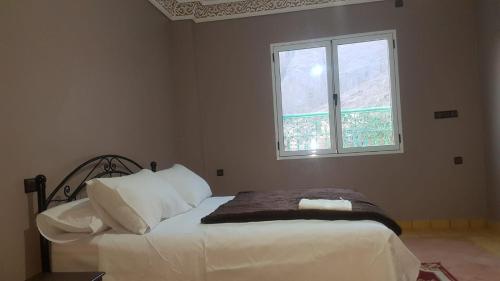 a bedroom with a bed with white sheets and a window at Auberge Restaurant Fatihi Freres in Tinerhir