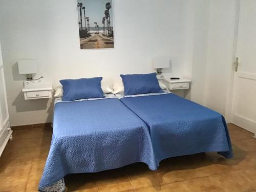 ein blaues Bett in einem weißen Zimmer mit 2 Tischen in der Unterkunft Apartamentos Playamar in La Playa Calera