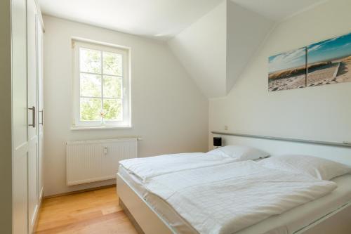 a white bedroom with a bed and a window at Mädesüß 02 in Ahrenshoop