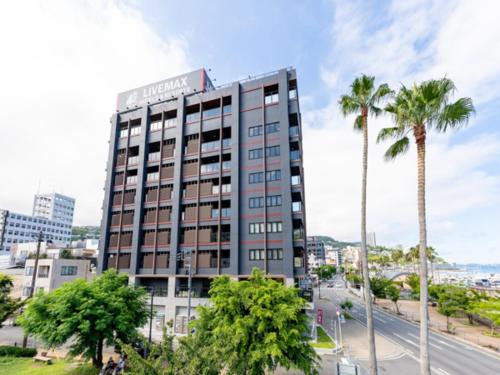 a tall building with palm trees in front of a street at LiVEMAX RESORT Atami OCEAN in Atami
