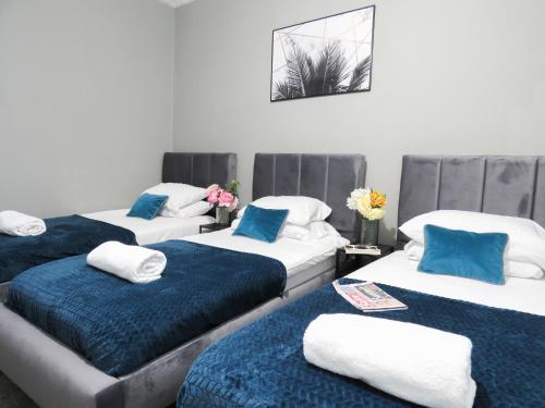 three beds in a room with blue and white pillows at Tudors eSuites 3 Bedroom House With Garden in Parkside