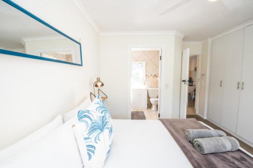 ein weißes Schlafzimmer mit einem Bett und einem Spiegel in der Unterkunft Seven River Club Mews in Plettenberg Bay