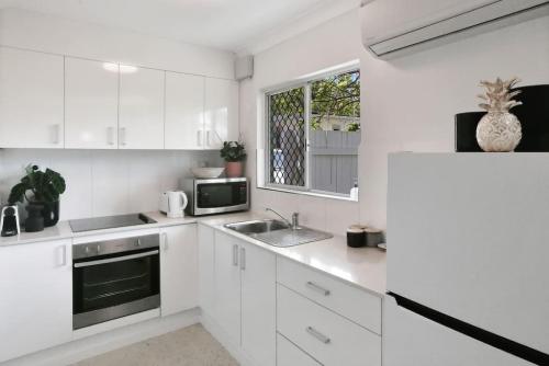 eine weiße Küche mit Spüle und Mikrowelle in der Unterkunft The Tropicana Courtyard in Cairns North