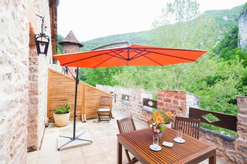 an orange umbrella on a patio with a table at Château De La Caze Piscine & Spa - Ste Enimie in Sainte-Énimie