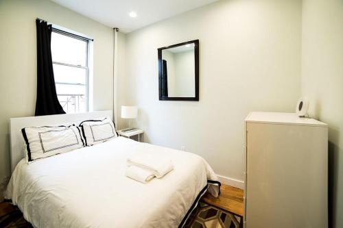 a bedroom with a bed with white sheets and a mirror at NEWLY RENOVATED HEART OF LOWER EAST SIDE 2BR 1BA, 5 MIN WALK TO SOHO, 1 BLOCK TO WHOLE FOODS, WASHER DRYER! in New York