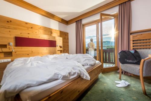 a bedroom with a bed and a chair and a window at Hotel Berghof in Ramsau am Dachstein