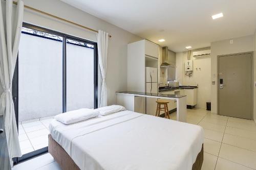 a bedroom with a large white bed and a kitchen at Pleione Flats in Curitiba
