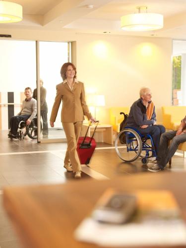 a woman walking through a lobby with a woman in a wheelchair at Heidehotel Bad Bevensen in Bad Bevensen