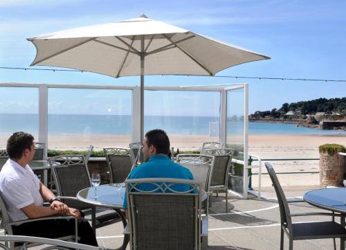 Due uomini seduti a un tavolo sotto un ombrellone in spiaggia di Beau Rivage a St Brelade