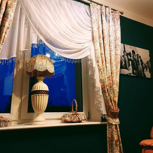 a window with a white curtain and a lamp on a shelf at Willa Zamkowisko in Gołubie