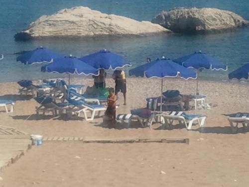 een groep blauwe parasols en stoelen op een strand bij Anastasia Studios, Apartments & Suites in Archangelos