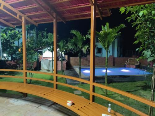 a wooden bench in front of a pool at night at Karjat - 3 BHK Private Bungalow with Private Pool & Garden in Karjat