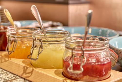 three jars of jam on a cutting board with spoons at Kurpension Freudenstein in Bad Füssing