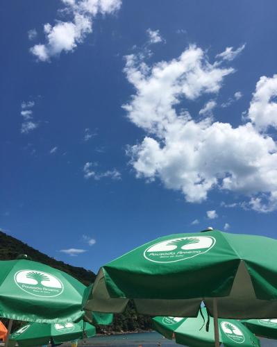 two green umbrellas on a beach with a blue sky at Pousada Aroeira in Barra do Sahy