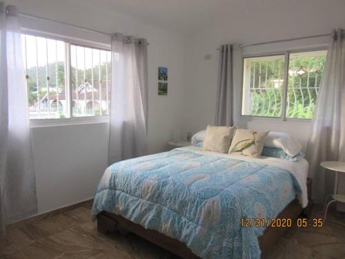 um quarto com uma cama e duas janelas em Pelicano Tropical Paraiso Samana em Santa Bárbara de Samaná