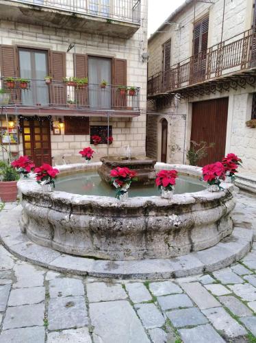 a stone fountain with red flowers in a courtyard at La Casa del Poeta , un romantico chalet da mille e una notte in Petralia Soprana
